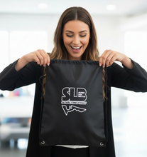 Load image into Gallery viewer, Woman holding a black drawstring bag with a logo and text on it.