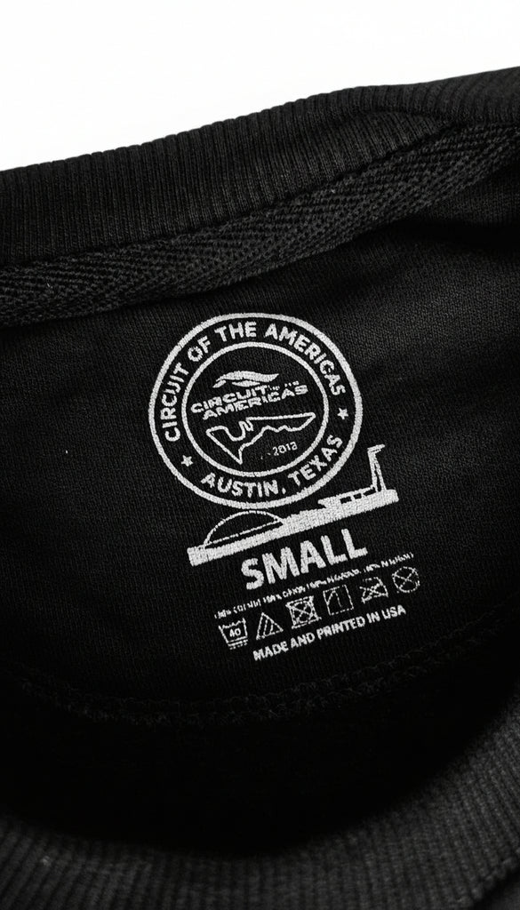 Close-up of a label on a black sweater with branding and text.