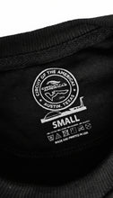 Load image into Gallery viewer, Close-up of a label on a black sweater with branding and text.